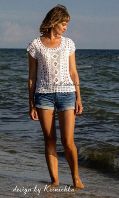 a beautiful young woman standing on top of a sandy beach next to the ocean with her feet in the water