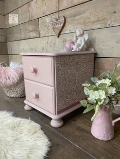 a pink dresser sitting on top of a wooden floor next to a vase with flowers