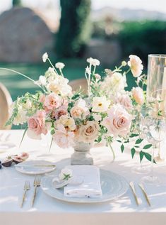 an arrangement of flowers in a vase on top of a table with silverware and wine glasses