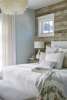 a white bed sitting under a window next to a wooden headboard and lamp in a bedroom