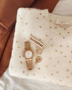 a sweater, watch and bracelet laying on top of a bed next to a pillow