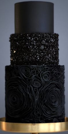 a three tiered black and gold wedding cake with flowers on it's side