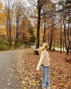 a woman walking down a leaf covered road