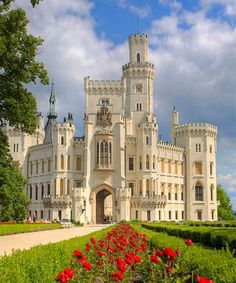 a large white castle sitting on top of a lush green field filled with red flowers