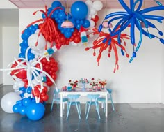 balloons and streamers are hanging from the ceiling above a table with chairs in front of it