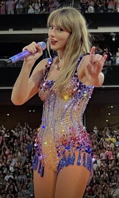 taylor swift performing at a concert in front of an audience with her hand up to the microphone