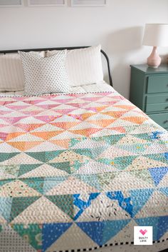 a bed with a colorful quilt on top of it next to a night stand and lamp