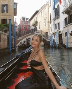 a woman sitting on the back of a boat in a canal with buildings around her