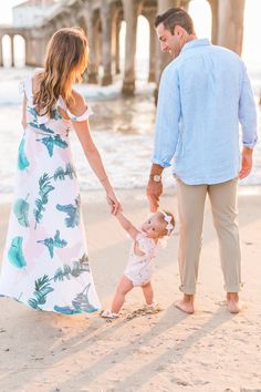 a man and woman hold hands as they walk along the beach with their toddler