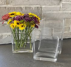 two clear vases filled with yellow and purple flowers