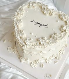 a heart shaped cake with the word happy written on it, sitting on a white tablecloth