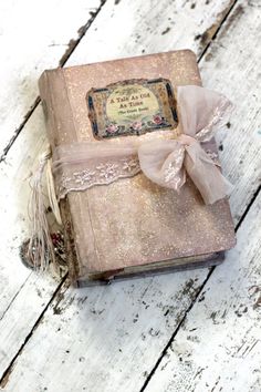 an old pink book with a bow on the front is sitting on a wooden surface