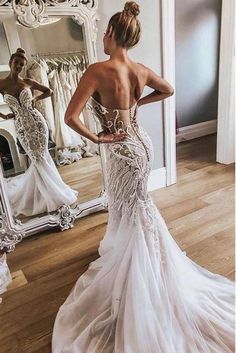 a woman in a wedding dress looking at herself in the mirror with her back to the camera