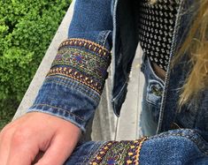 a close up of a person's hand holding something in their left hand and wearing a blue jean jacket with an embroidered design on it