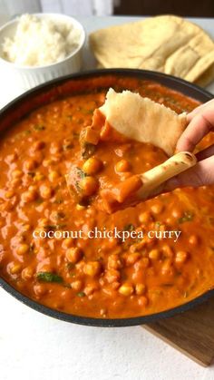 a hand holding a tortilla chip and dipping it into a bowl of beans