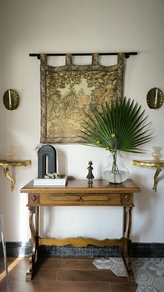 a wooden table topped with a vase filled with green plants next to a painting on the wall