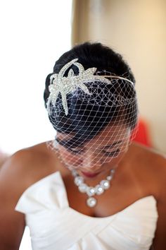 a woman in a wedding dress wearing a birdcage veil with pearls on her head