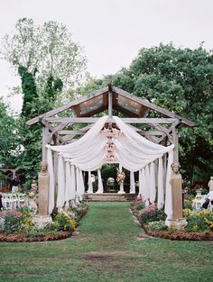 an outdoor wedding ceremony with white drapes and flowers