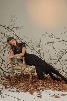 a woman sitting on top of a chair in the snow next to trees and branches