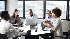 a group of people sitting around a table with laptops and papers in front of them