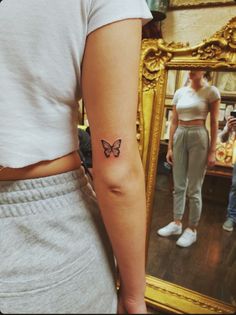 a woman with a butterfly tattoo on her left arm, standing in front of a mirror