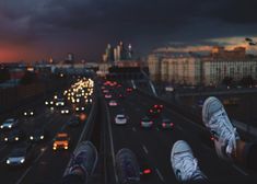 someone's feet are standing on the edge of a high rise over a busy highway