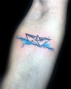 a watercolor tattoo with an origami paper boat on the left arm and blue ink