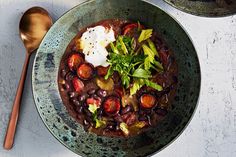 a bowl filled with beans and vegetables on top of a table next to a spoon