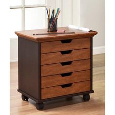 a wooden desk with drawers on wheels and pencils in the bottom drawer that is open