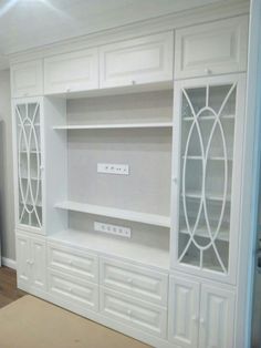 a white entertainment center with glass doors and drawers in a room that is painted white