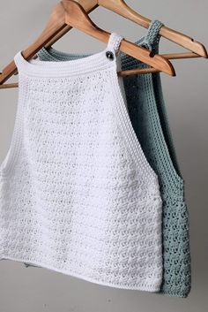 two crocheted tops hanging on a wooden hanger next to each other, one in white and the other in blue