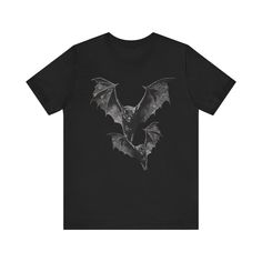 Venture into the darkness with this cool tee featuring a bold illustration of two bats. Ideal for fans of dark academia, goth, punk, or Halloween. xo Bella+Canvas unisex short sleeve tees are made with 100% Airlume combed and ring-spun cotton. All its products are manufactured in the US and internationally in a humane sustainable way and is part of the Fair Labor Association as well as Platinum WRAP certified. SIZING * Bella + Canvas 3001 t-shirts are unisex and fit true to size. * Women wanting a slim fit should go down a size. * For an oversized fit, please order up 1 or 2 sizes. * For the best fit, measure one of your favorite fitting t-shirts before checking the size chart. * Link for Women's-fit tee below. CARE INSTRUCTIONS * Machine wash cold, inside-out, gentle cycle with similar co Alt Shirts, Black Halloween T-shirt For Alternative Fashion, Emo Halloween T-shirt For Alternative Fashion, Gothic Short Sleeve Halloween T-shirt, Gothic T-shirt With Graphic Print, Bold Illustration, Goth Vampire, Grunge Tee, Bat Shirt