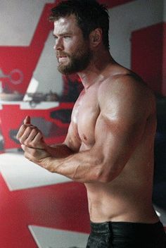 a shirtless man standing in front of a red and white wall with his arms crossed