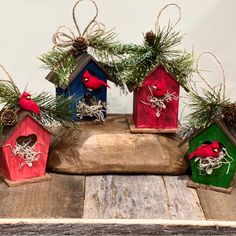 four birdhouses are decorated with pine cones and red cardinals on top of them