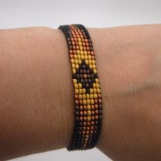 a person's arm with a bracelet on it that has an orange, yellow and black bead design