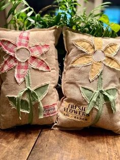 two pillows with flowers on them sitting on a wooden table next to a potted plant