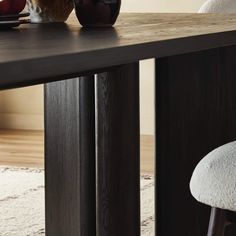 a wooden table with two vases on it and a white chair in the background