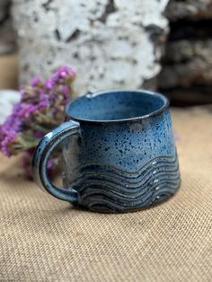 a blue mug sitting on top of a table next to purple flowers and rock formations