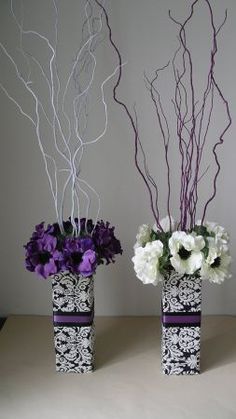 two vases with purple and white flowers in them on a table next to each other