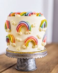 a white cake with rainbows and clouds on top is sitting on a metal stand