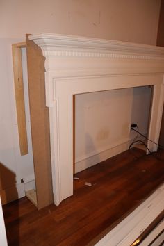 an empty room with a white fireplace and wood flooring in the middle of it