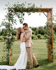 a bride and groom kissing in front of an outdoor wedding ceremony arch with greenery