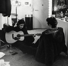 two women sitting on the floor playing guitars in a room with coca - cola machines