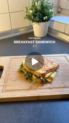 a sandwich sitting on top of a wooden cutting board next to a potted plant