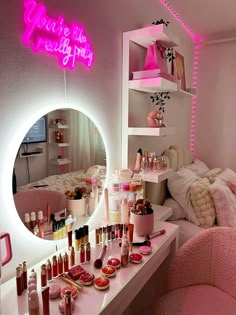 a vanity with pink lights and lots of makeup on the counter in front of a mirror