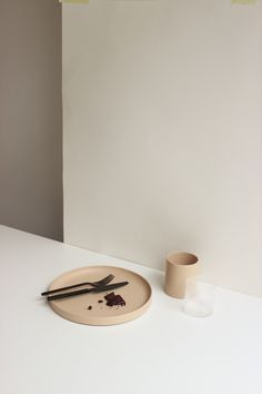 a white table with a plate, fork and knife on it next to a cup