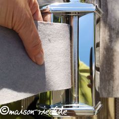 a person holding something in their hand near a metal object that is reflecting the sky