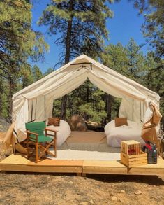 a tent set up in the middle of a forest with two chairs and a table