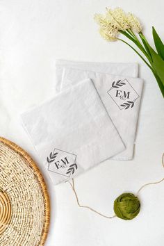 two napkins with the word em on them next to some yarn and flowers in a basket