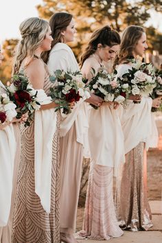 a group of women standing next to each other holding bouquets in their hands and wearing long dresses